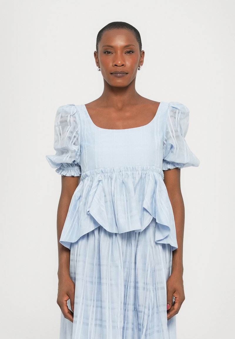 Vaaleansininen mekko, jossa on neliönmuotoinen pääntie, puffatut lyhyet hihat ja peplum-muotoilu. Kankaan pinnassa on hienovarainen ruutukuosi ja pehmeä tekstuuri.
