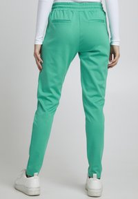 Rohelised dressipüksid pehmest kangast, millel on elastne vööde, kaks tagataskut ja kitsenevad sääred, kombineeritud valgete tossudega.