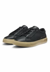 Black leather sneakers with a textured upper, featuring elongated laces and a beige rubber sole. Minimalist design with no visible branding.