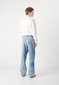 Light blue, loose-fitting denim pants with patches and embroidery, including a smiley face and logo details. High waist and wide legs.