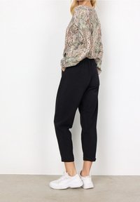 Blusa verde a maniche lunghe, morbida, con motivo paisley abbinata a pantaloni neri affusolati e scarpe da ginnastica bianche.