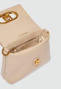 Sac à main en cuir beige avec une finition texturée, quincaillerie dorée, fermeture magnétique et poche intérieure zippée. Logo de la marque en relief à l'intérieur.