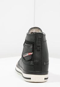 Czarne skórzane sneakersy typu high-top, z przeszywanym wierzchem, naszywką z logo i białą gumową podeszwą z czarnymi paskami. Teksturowana tylna część.