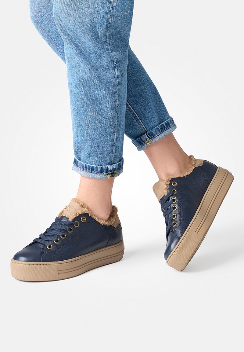 Baskets bleu marine avec doublure en fourrure beige, semelle plate beige et œillets dorés. Présentent un bout rond et un design classique à lacets.