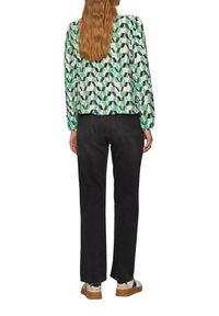 Langarm blouse met een geometrisch patroon in groen, zwart en wit, gecombineerd met donker rechte jeans en casual sneakers.