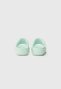 Light mint green sandals with a sleek design, open back, rounded heel, and textured outsole. Features subtle branding on the side.