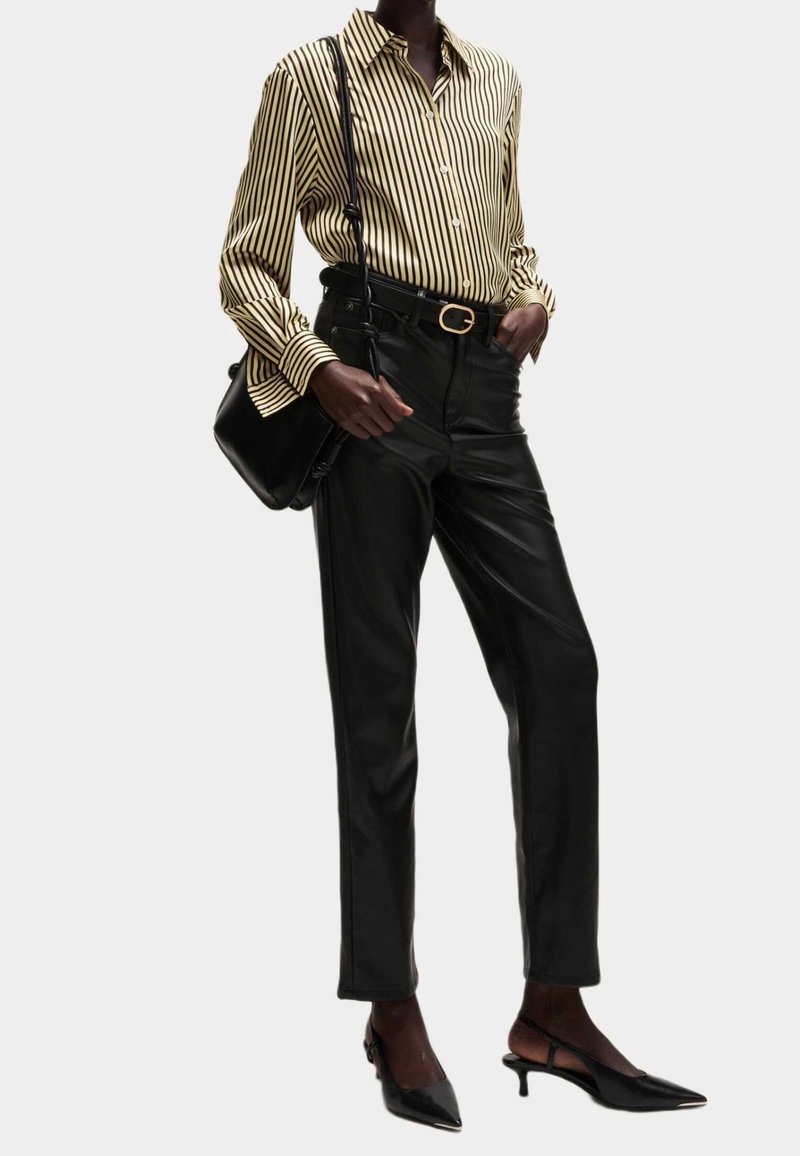 Chemise à rayures jaune et noire, associée à un pantalon en simili cuir noir et des talons aiguilles. Les accessoires incluent un sac noir.
