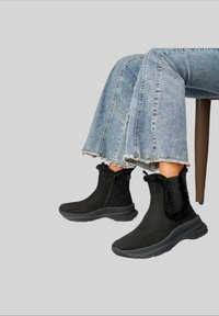 Bottes noires à chevilles avec un bord doublé de fourrure, fermeture éclair latérale, et semelle en caoutchouc texturée. Portées avec un jean bleu clair déchiré aux ourlets.