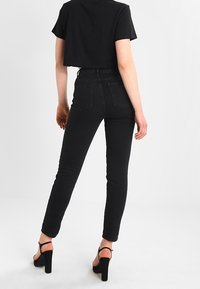 T-shirt nera cropped abbinata a jeans skinny neri a vita alta. I jeans presentano una texture liscia e pochi dettagli. Sandali neri con tacco completano il look.