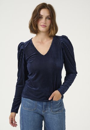 Navy blue V-neck blouse made of textured fabric with vertical stripes, featuring puffed sleeves and a fitted design, paired with blue jeans.
