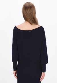Pulover tricotat de culoare albastru marin, cu un design off-the-shoulder, mâneci lungi și un tiv dublu. Include un mic detaliu argintiu în partea din spate.
