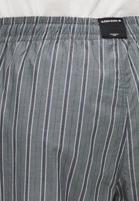 Grijs gestreepte boxershorts met elastische tailleband. Bevat smalle witte verticale strepen en een zwart merketiket op de tailleband.