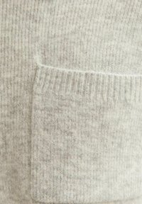 Maglione a maglia grigio chiaro con una texture a coste, una tasca visibile e un tessuto morbido e peloso. I dettagli includono una leggera variazione nella tonalità.