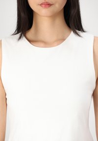 Débardeur blanc sans manches avec un col rond, texture lisse et silhouette ajustée, idéal pour être porté en superposition ou seul.