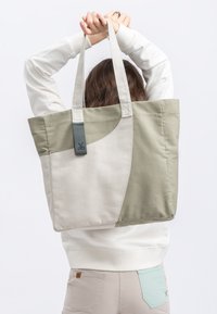 Tote bag met crèmekleurige en olijfgroene panelen, rechthoekige vorm, voorzien van stevige hengsels en een getextureerde accenttag in het groen.