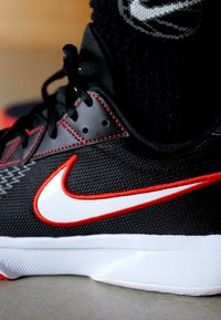 Sort træningssko med hvid og rød Nike-logo, rød syning og sorte snørebånd, båret med sorte sokker.