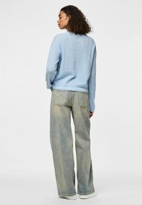 Himmelblauer Strickpullover mit geripptem Saum und langen Ärmeln, kombiniert mit ausgewaschenen, weit geschnittenen Jeans mit hoher Taille und rohem Saum.