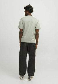 Camiseta de algodón verde claro con mangas cortas y cuello redondo, combinada con pantalones de pierna ancha negros y zapatillas blancas. Diseño sencillo, sin patrones.