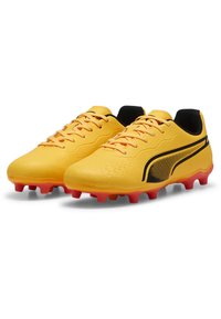 Geltonos futbolo batai su tekstūruotu viršumi, juodomis akcento juostelėmis ir raudonais kaliošais ant pado. Yra raištelių dizainas ir paminkštinta apykaklė.