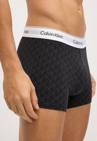 Czarne slipki bokserskie z geometrycznym wzorem, elastyczny pas Calvin Klein, dopasowany krój, miękka tekstura, długość do połowy uda oraz minimalna ilość szwów.