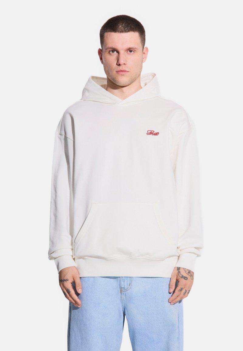 Biała bluza z kapturem i przednią kieszenią oraz czerwonym logo "Frost". Miękka tkanina, luźny krój i regulowany kaptur ze sznurkiem. Noszona z jasnoniebieskimi dżinsami.