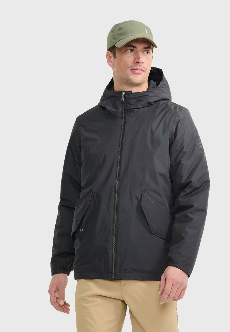 Schwarze Zip-Jacke mit Kapuze, ausgestattet mit zwei Fronttaschen, aus glattem Stoff. Getragen mit einer hellgrünen Mütze.