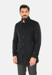 Cappotto in lana blu scuro con colletto alto, bottoni frontali e tasche laterali. Presenta una vestibilità su misura e un tessuto texturizzato.