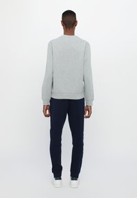 Sudadera gris de manga larga, con puños y dobladillo acanalados, combinada con pantalones azul marino. El modelo está de espaldas frente a la cámara. Zapatillas deportivas blancas visibles.