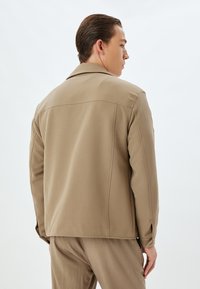 Beige jasje met een gladde textuur, klassieke kraag en knoopmanschetten, met nauwkeurig afgewerkte naden en een licht-lose pasvorm.