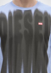 Blaues und schwarzes Batik-Shirt mit großen schwarzen Buchstaben und einem kleinen roten Diesel-Logo auf der oberen linken Brust.