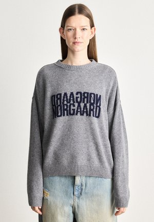 Grå stickad tröja med sänkta axlar, med en mörkblå "Nørgaard" logotyp över bröstet. Ribbad halsringning och fåll.