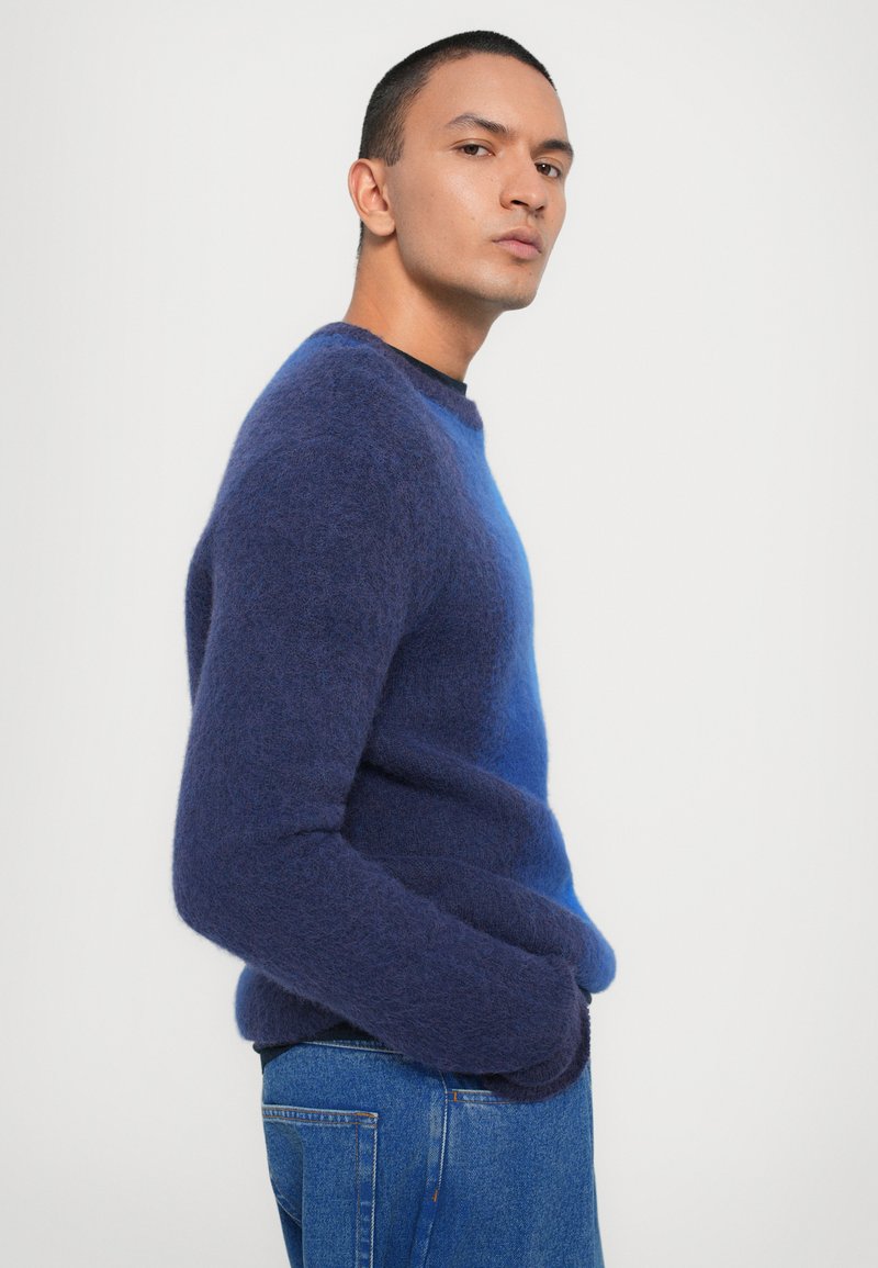 Blue gradient pullover sweater with a soft texture, round neckline, and long sleeves. Worn with classic denim jeans.