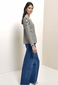 Striped long-sleeve shirt in black and white, paired with wide-leg blue jeans. Model stands against a light background, showcasing outfit details.