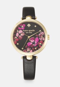 Reloj con correa de cuero negro y caja redonda en tono dorado, que presenta un diseño floral en rosa y púrpura sobre un fondo negro, y marcadores de hora dorados.