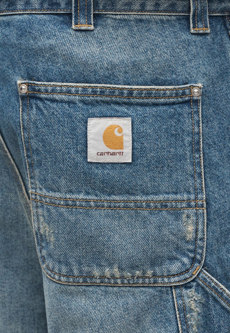 Denimshorts i lyseblå med en slidstærk tekstur. Har en baglomme med et hvidt mærke og en gul logo, forstærkede syninger.