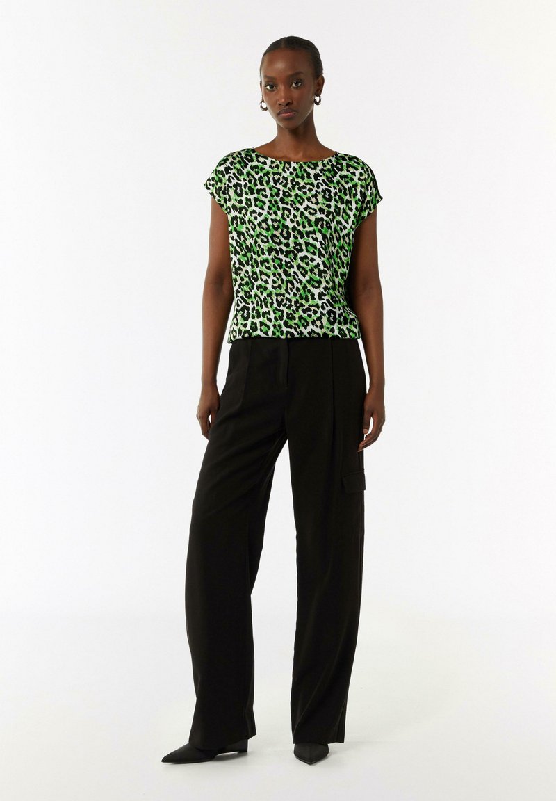 Groene luipaardprint korte mouwen top met een ontspannen pasvorm, gecombineerd met zwarte wijde broekspijpen en puntige zwarte schoenen. Soepele stoftextuur.