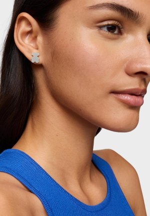 Orecchino a perno a forma di orso in argento esposto sull'orecchio di un modello, caratterizzato da una superficie liscia e un design minimalista in un colore neutro.