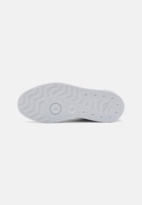 Hvit gummisåle til sneaker med bølgete mønster og sirkulært dempelement. Teksturert grip-seksjoner forbedrer grepet.