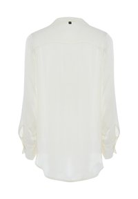 Blusa color crema con maniche lunghe leggermente a sbuffo, orlo arrotondato e un colletto semplice. Tessuto liscio, senza motivi o accenti visibili.