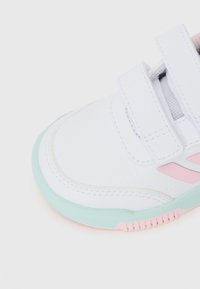 Valged tennisekad, millel on sile pind, rohelised tallad ja roosa aktsent. Omab Velcro rihmasid ja tekstureeritud külge lisatud haardeks.