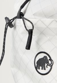Λευκή τσάντα από ύφασμα με σχέδιο διαμαντιού, που φέρει ένα μαύρο λογότυπο ενός μαμούθ και μαύρο κορδόνι για κλείσιμο. Διακοσμημένη με μαύρα μεταλλικά εξαρτήματα.