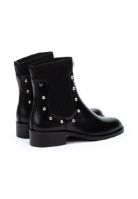 Botas negras de tobillo con punteras redondeadas, paneles laterales elásticos acanalados y tachuelas doradas decorativas en los lados exteriores. Tacones gruesos en bloque.