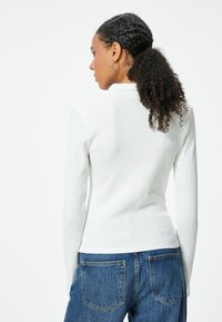 Top bianco a maniche lunghe con design aderente e colletto alto, abbinato a jeans blu a vita alta con tasche posteriori.