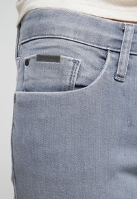 Světlé šedé džíny z denimu s přední kapsou, texturovanou tkaninou a černou nášivkou s logem "Calvin Klein Jeans".