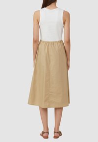 Beige midi skirt with an elastic waistband, made of smooth fabric; worn with a fitted white tank top and light brown sandals.