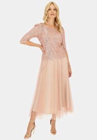 Kratek złoty top z cekinami i rękawami do trzy czwarte w zestawieniu z luźną, jasnoróżową spódnicą z tiulu. Kolor butów to beżowy.