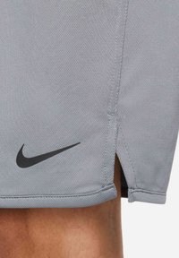 Šedé športové šortky vyrobené z texturovanej tkaniny, s čiernym logom Nike na boku a bočným rozparkom pre lepší pohyb.
