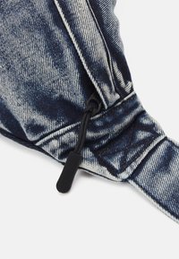 Denim-kangas, jossa on sininen ja valkoinen pesukuosi, ja näkyvissä musta vetoketjunvetäjä, joka on kiinnitetty saumaan näkyvine ompeleineen.