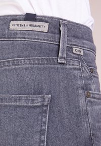 Jeans de mezclilla gris con una cintura de altura media, bolsillos traseros y etiqueta "Citizens of Humanity" cerca de la cinturilla. Detalles en hardware plateado.