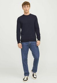 Navy knit sweater with a round neckline, paired with blue denim jeans and black and cream sneakers. Simple, fitted design with ribbed cuffs.